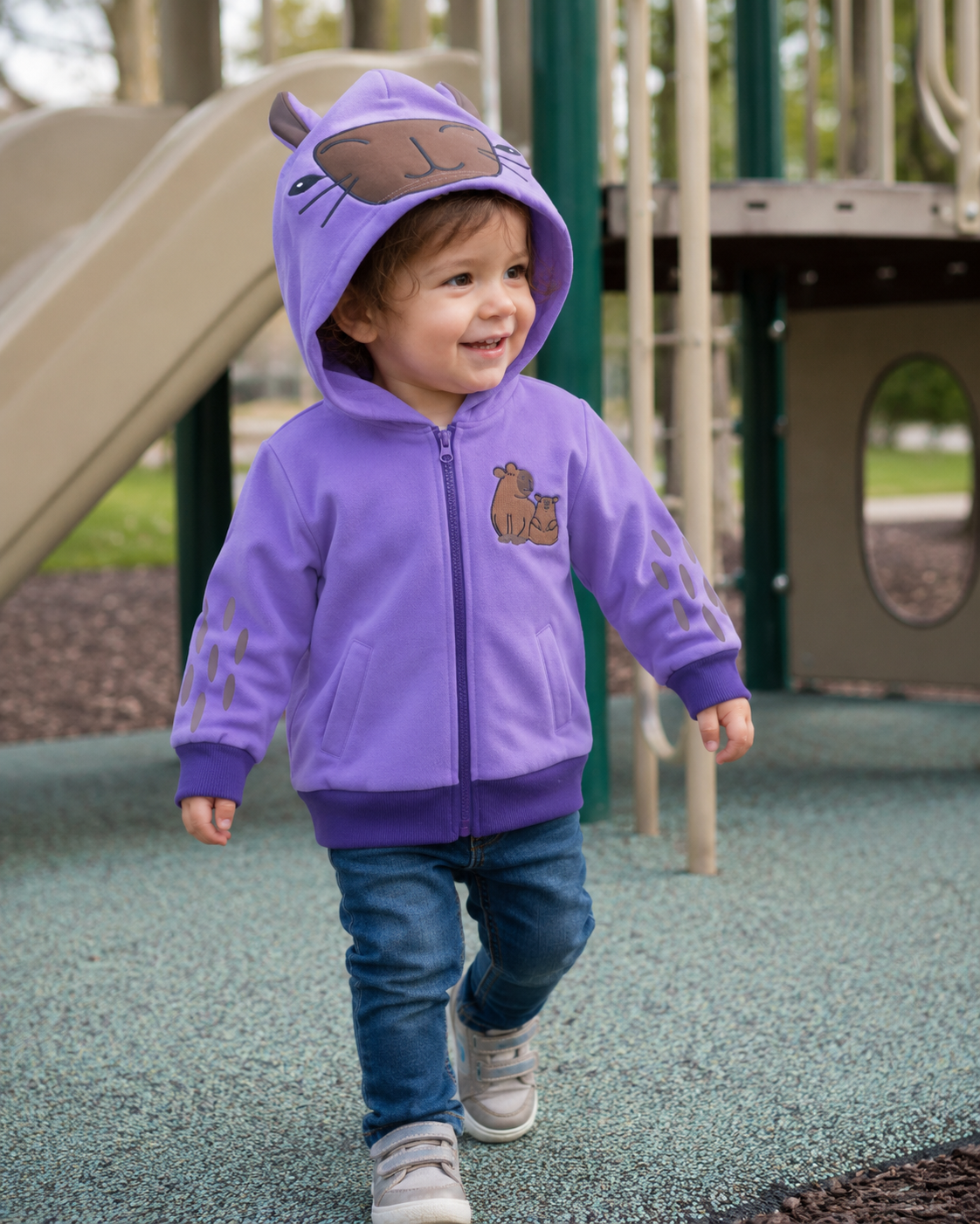 Child wearing the Lavender Sky capybara backpack hoodie on a playground